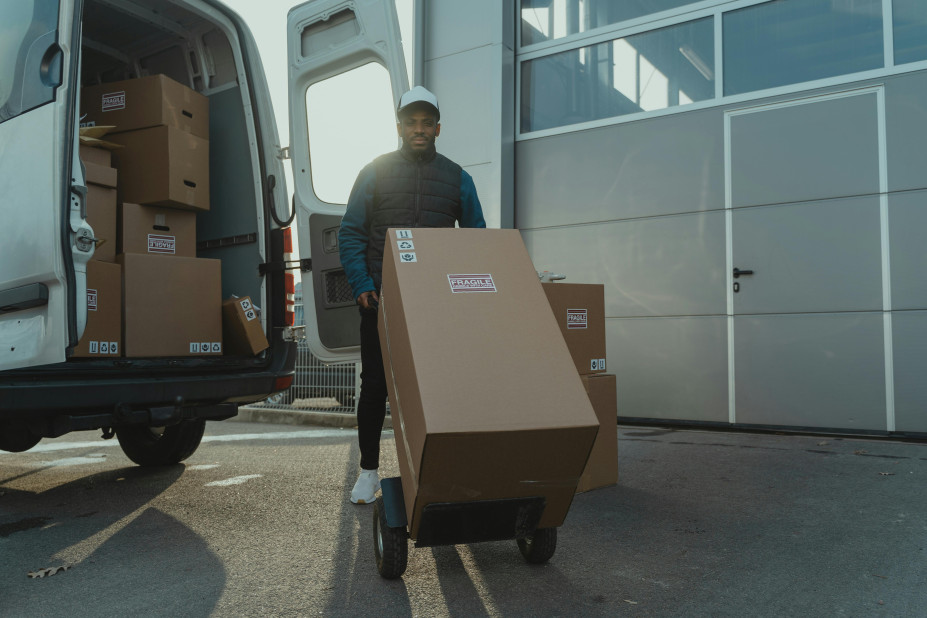 a person holding a trolly packed with boxes on it, loading in a car to shift goods.